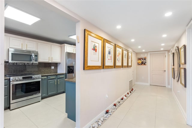 kitchen featuring light tile patterned flooring, white cabinetry, appliances with stainless steel finishes, dark stone counters, and decorative backsplash