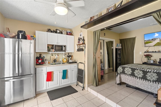 kitchen featuring appliances with stainless steel finishes, light tile patterned floors, white cabinets, and a textured ceiling