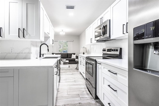 kitchen with white cabinetry, sink, light wood-type flooring, and appliances with stainless steel finishes