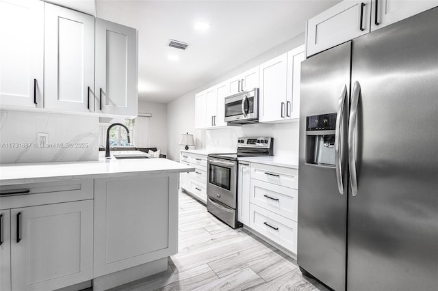 kitchen featuring sink, light hardwood / wood-style flooring, appliances with stainless steel finishes, white cabinets, and decorative backsplash