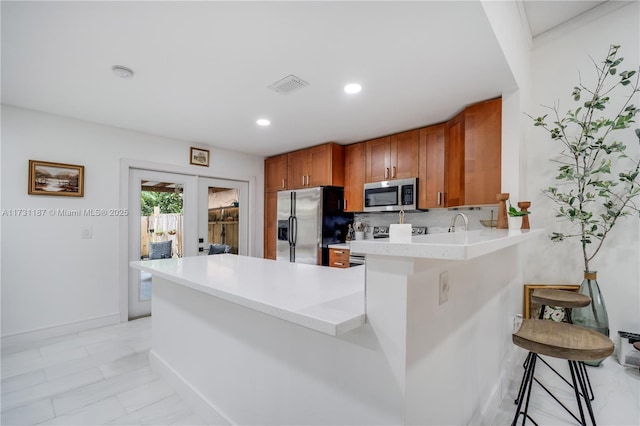 kitchen featuring french doors, appliances with stainless steel finishes, a kitchen breakfast bar, kitchen peninsula, and decorative backsplash