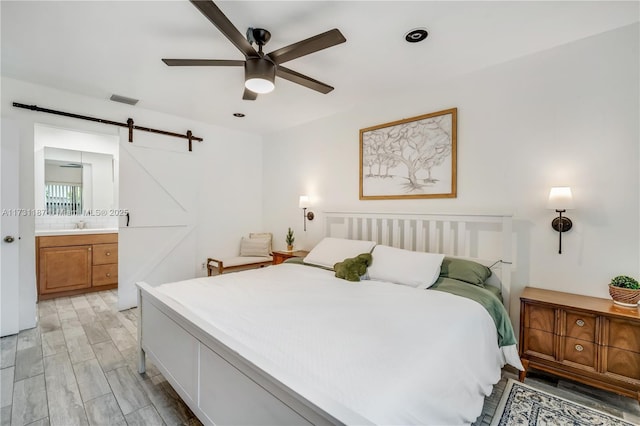 bedroom featuring connected bathroom, sink, light wood-type flooring, ceiling fan, and a barn door