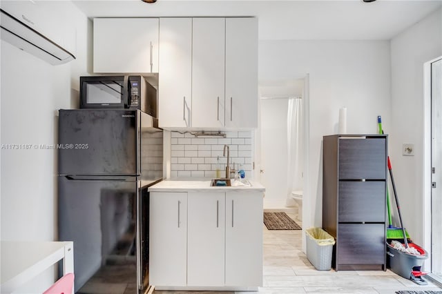 kitchen with a wall mounted air conditioner, white cabinetry, sink, decorative backsplash, and black appliances