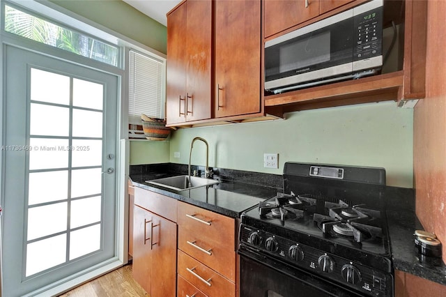 kitchen featuring black gas stove, sink, dark stone countertops, and light wood-type flooring