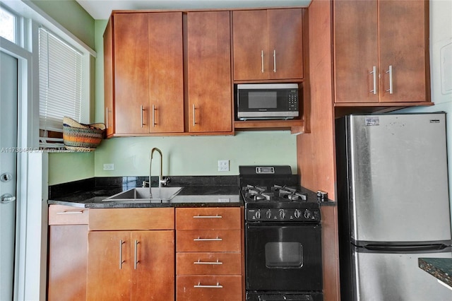 kitchen featuring built in microwave, sink, dark stone countertops, stainless steel refrigerator, and black gas range