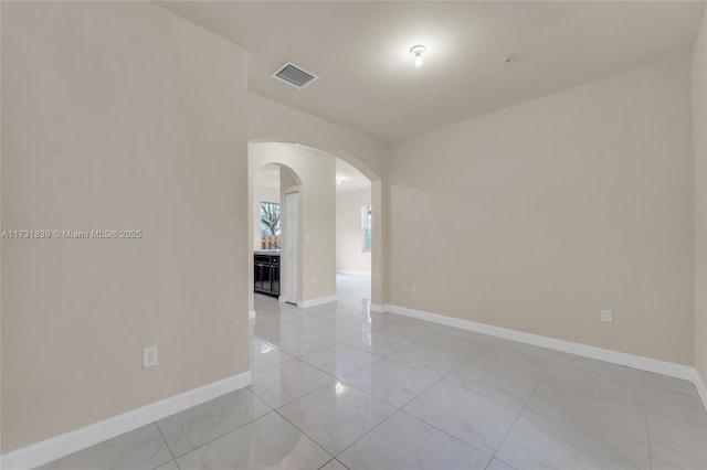 unfurnished room featuring arched walkways, marble finish floor, visible vents, and baseboards