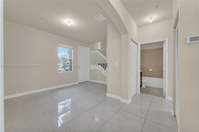 interior space featuring baseboards, arched walkways, visible vents, marble finish floor, and stairs