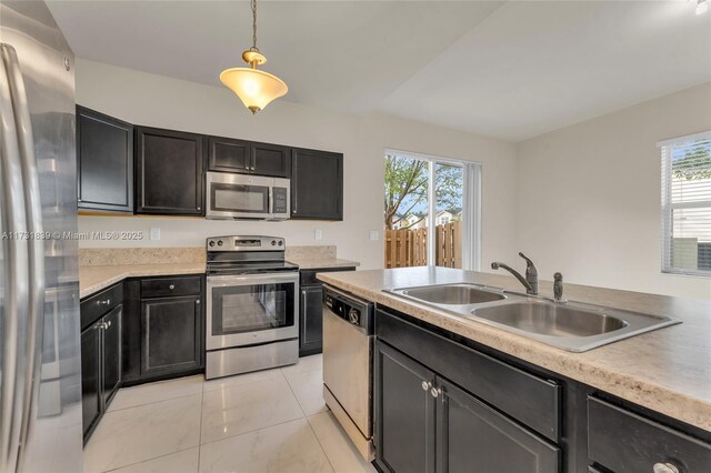 kitchen with appliances with stainless steel finishes, hanging light fixtures, a sink, light countertops, and a wealth of natural light