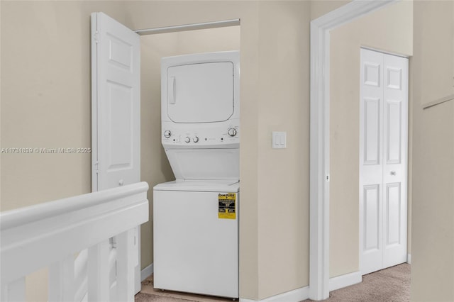 laundry area featuring light carpet, stacked washing maching and dryer, baseboards, and laundry area