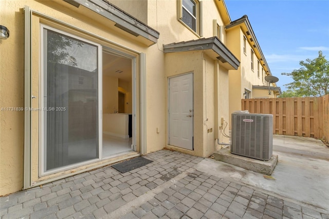 view of exterior entry with a patio area, fence, central AC, and stucco siding