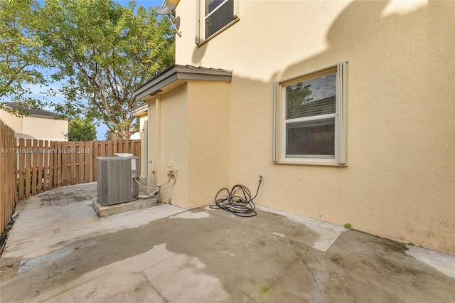 view of side of property featuring cooling unit, stucco siding, fence, and a patio