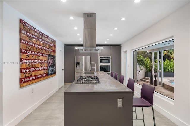 kitchen with gray cabinets, a kitchen breakfast bar, island exhaust hood, a kitchen island with sink, and stainless steel appliances