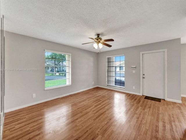 empty room with ceiling fan, a wealth of natural light, a textured ceiling, and light hardwood / wood-style flooring