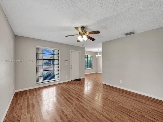 empty room featuring ceiling fan with notable chandelier, hardwood / wood-style floors, and a textured ceiling