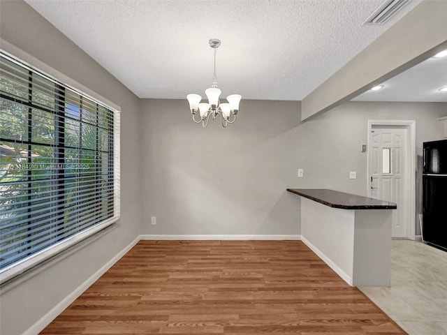 unfurnished dining area with a chandelier, a textured ceiling, and light wood-type flooring