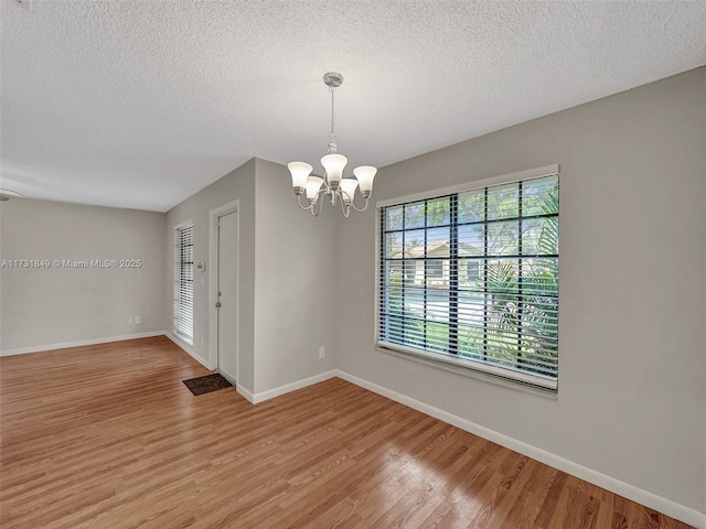 unfurnished room with an inviting chandelier, light hardwood / wood-style floors, and a textured ceiling