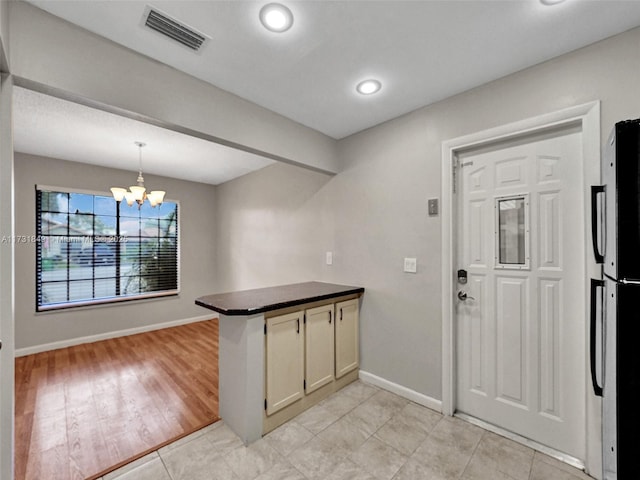 kitchen featuring black refrigerator, hanging light fixtures, light tile patterned flooring, kitchen peninsula, and a chandelier