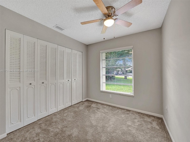 unfurnished bedroom featuring a closet, ceiling fan, light colored carpet, and a textured ceiling