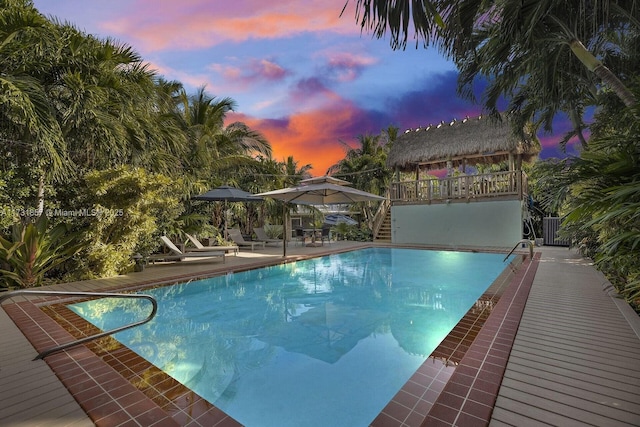 pool at dusk with a gazebo, a patio area, and cooling unit