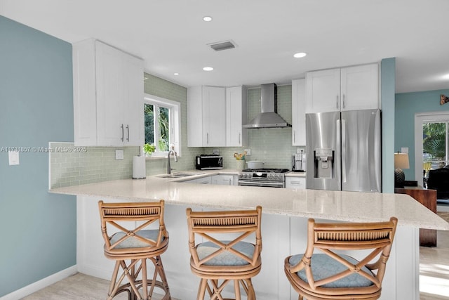 kitchen featuring wall chimney range hood, sink, a breakfast bar area, appliances with stainless steel finishes, and kitchen peninsula