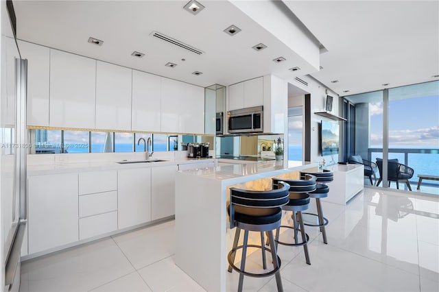 kitchen featuring light tile patterned flooring, a center island, white cabinets, and a water view