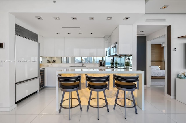 kitchen featuring wine cooler, white built in refrigerator, a breakfast bar, light tile patterned floors, and white cabinets