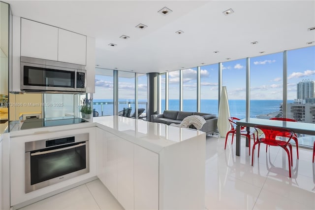 kitchen featuring light tile patterned flooring, a water view, appliances with stainless steel finishes, and white cabinets