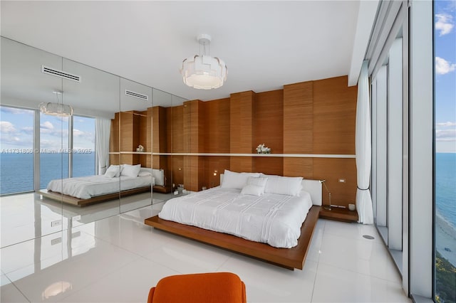 bedroom featuring wood walls, light tile patterned floors, access to exterior, floor to ceiling windows, and a water view