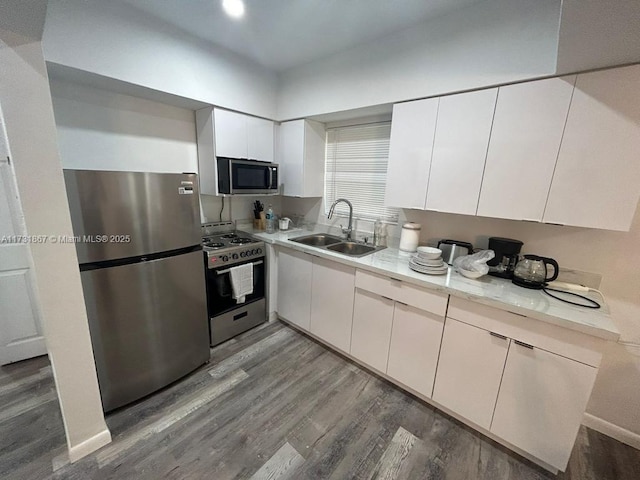 kitchen with appliances with stainless steel finishes, white cabinetry, sink, hardwood / wood-style flooring, and light stone counters