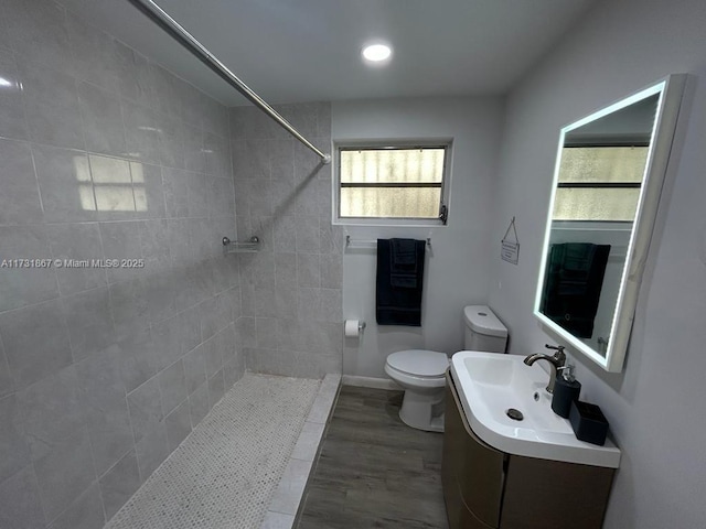 bathroom with tiled shower, vanity, toilet, and wood-type flooring