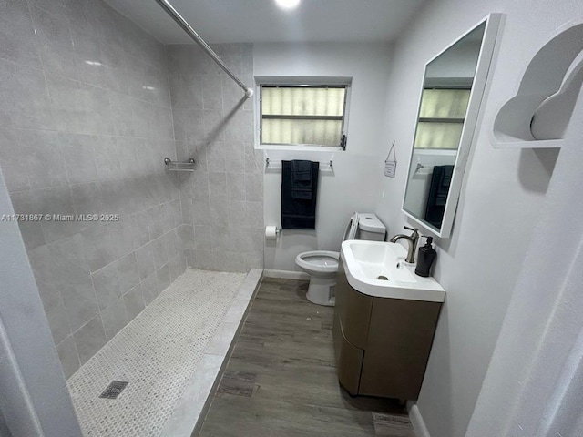 bathroom featuring vanity, tiled shower, hardwood / wood-style floors, and toilet