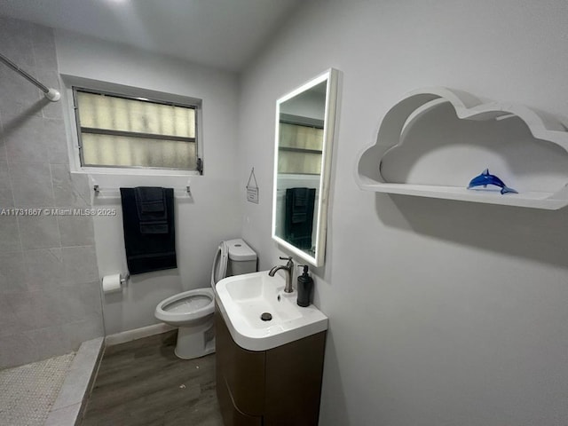 bathroom featuring vanity, hardwood / wood-style floors, toilet, and tiled shower