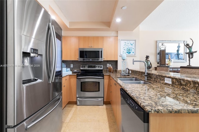 kitchen with sink, appliances with stainless steel finishes, dark stone countertops, a tray ceiling, and decorative backsplash