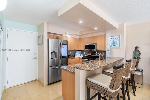 kitchen with dark stone countertops, stainless steel appliances, tasteful backsplash, a kitchen bar, and kitchen peninsula