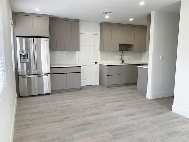 kitchen with sink, stainless steel fridge, gray cabinetry, light hardwood / wood-style floors, and decorative backsplash