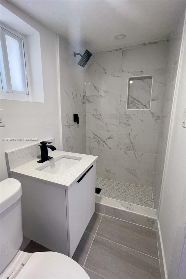 bathroom with vanity, toilet, and a tile shower