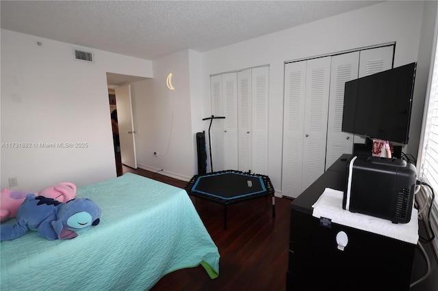 bedroom with dark wood-type flooring, a textured ceiling, and two closets