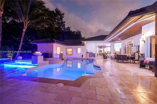 pool at dusk featuring an in ground hot tub and a patio