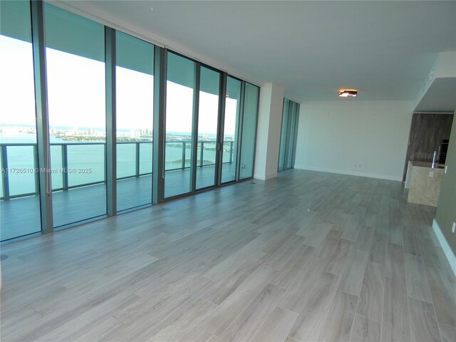 spare room with a water view, a wall of windows, and light hardwood / wood-style floors