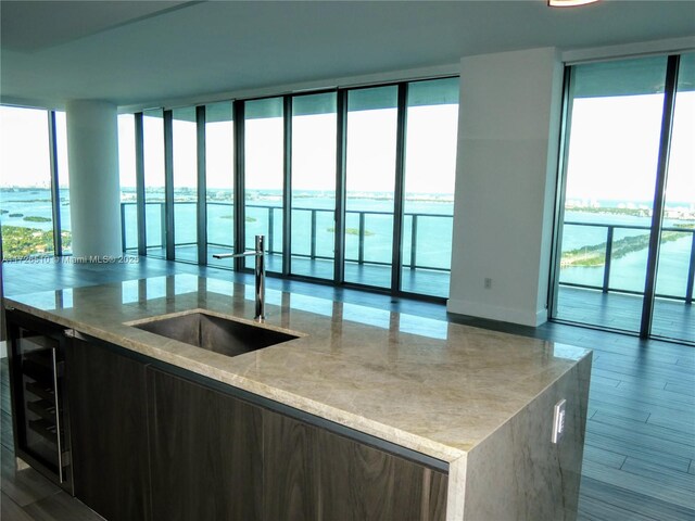 kitchen with a water view, sink, wine cooler, and light stone counters