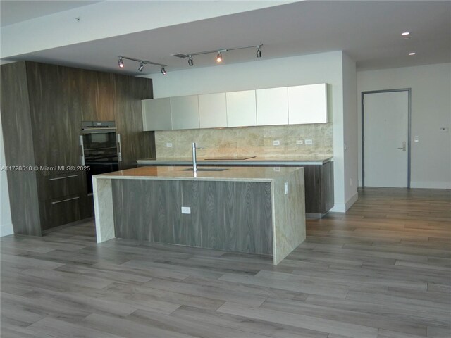 kitchen featuring sink, white cabinetry, double oven, an island with sink, and backsplash