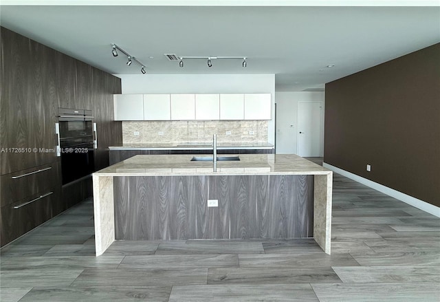 kitchen with rail lighting, a sink, modern cabinets, a kitchen island with sink, and white cabinetry