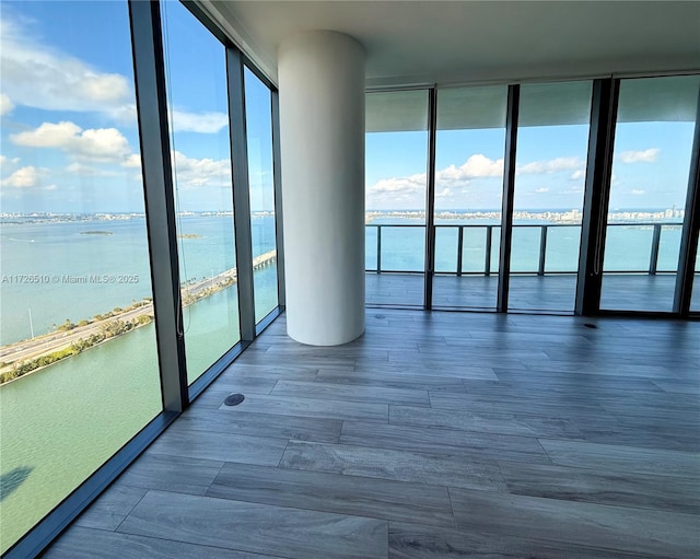 empty room with a wall of windows, wood finished floors, a water view, and a wealth of natural light