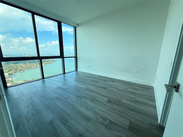 spare room with expansive windows, baseboards, wood finished floors, and a water view