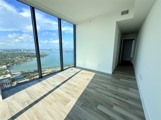 empty room featuring wood finished floors, visible vents, a water view, baseboards, and expansive windows