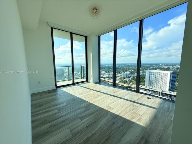empty room with wood finished floors, a city view, expansive windows, and baseboards