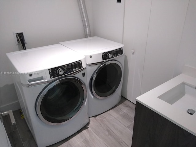laundry room featuring independent washer and dryer, light wood-style flooring, a sink, and laundry area