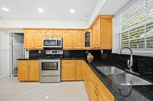 kitchen featuring sink, light tile patterned floors, appliances with stainless steel finishes, backsplash, and dark stone counters