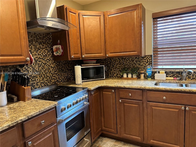 kitchen with wall chimney range hood, stainless steel stove, sink, tasteful backsplash, and light stone countertops