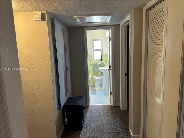 corridor featuring tile walls, a textured ceiling, and dark colored carpet